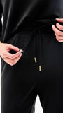 Person wearing black pants with a drawstring and gold zipper on a white background