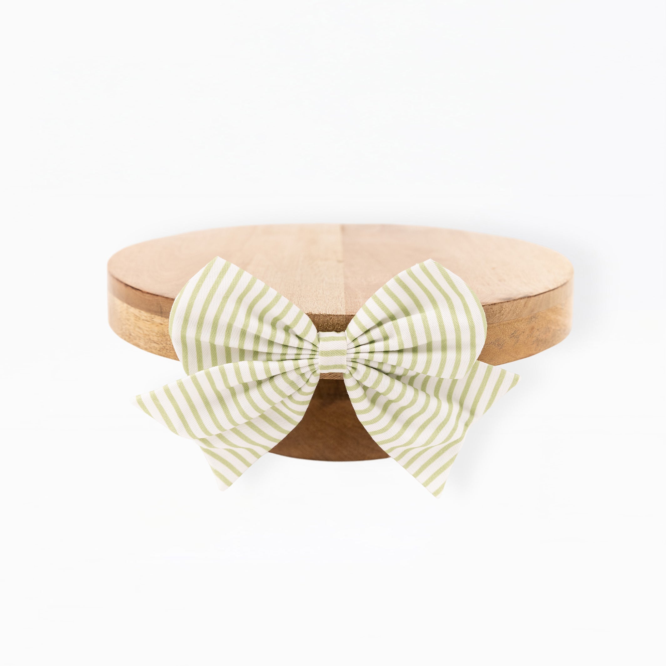 A light green and white striped bow tied around a round natural wood tray, photographed against a solid white background.
