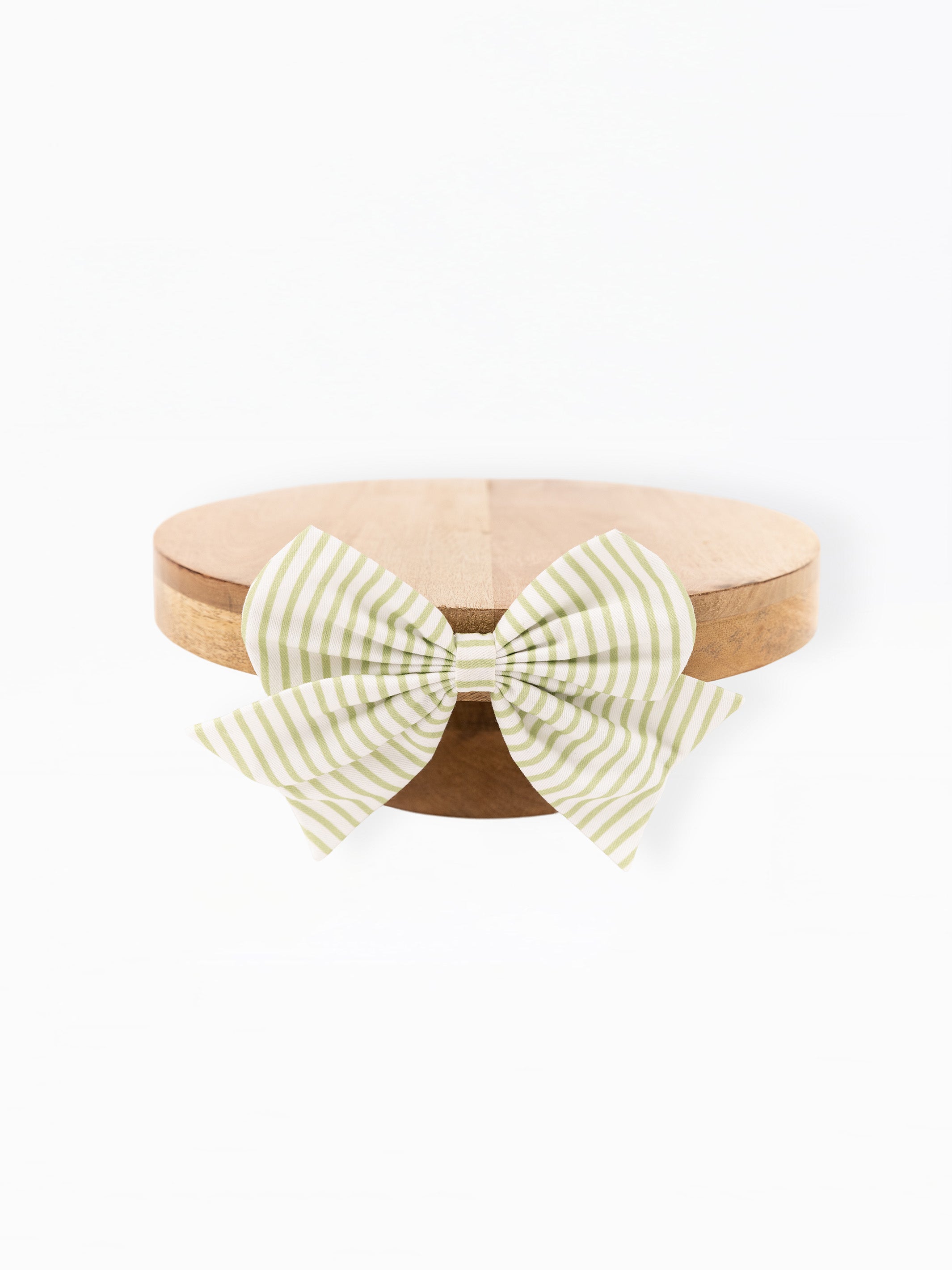 A light green and white striped bow tied around a round natural wood tray, photographed against a solid white background.