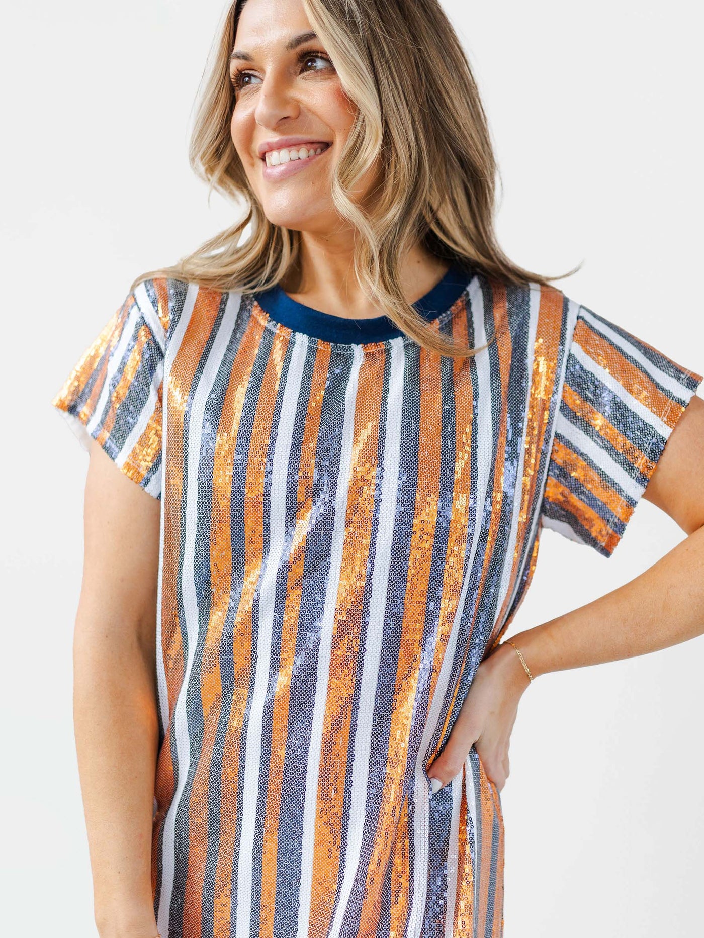 Woman wearing a striped navy and orange sequin dress on a plain background