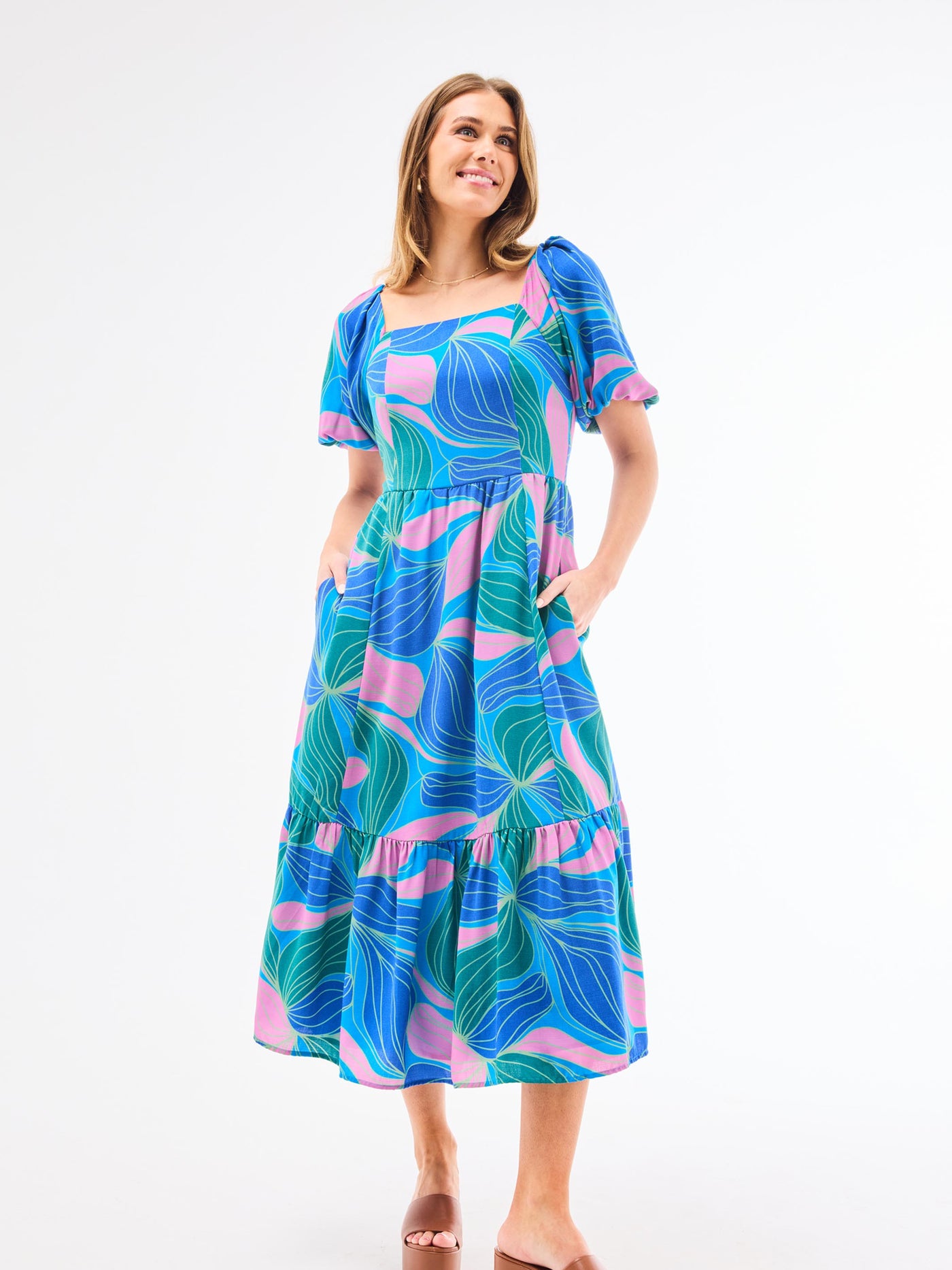 A model wearing a midi-length Alexi Dress in a vibrant blue and green floral pattern with a square neckline and puff sleeves.