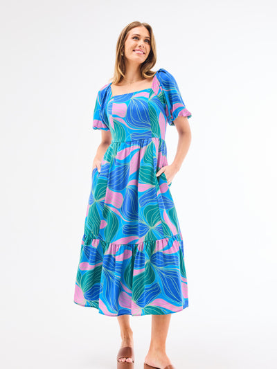 A model wearing a midi-length Alexi Dress in a vibrant blue and green floral pattern with a square neckline and puff sleeves.