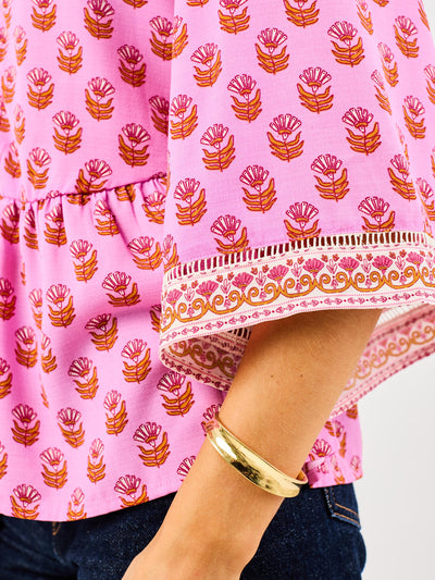 woman in floral pink, flowy blouse wearing dark blue jeans on a white background