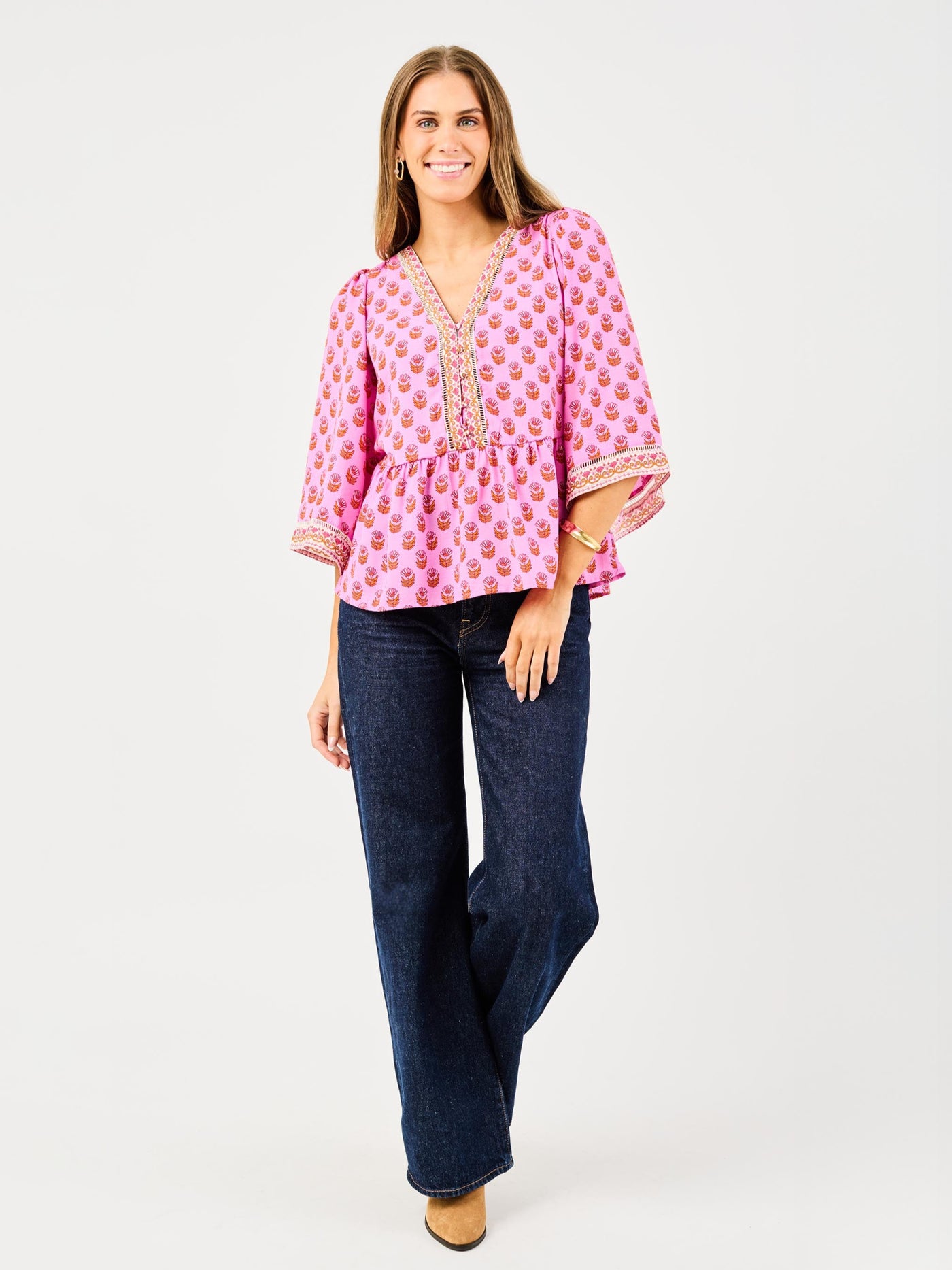 woman in floral pink, flowy blouse wearing dark blue jeans on a white background