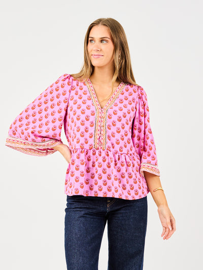 woman in floral pink, flowy blouse wearing dark blue jeans on a white background