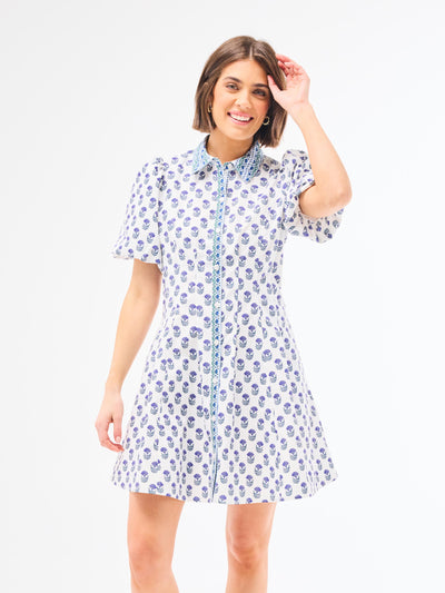 Woman wearing a dainty blue floral dress with a point collar and button front on a white background