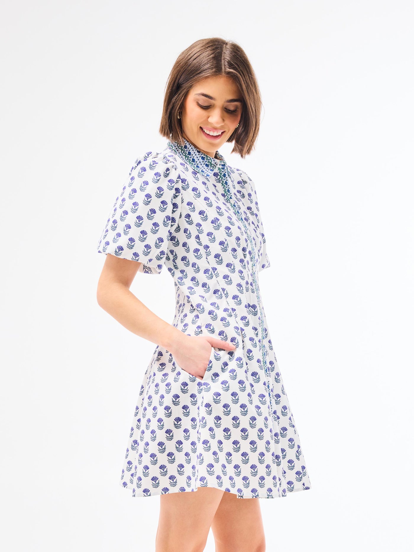 Woman wearing a dainty blue floral dress with a point collar and button front on a white background