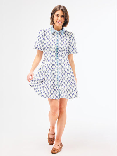 Woman wearing a dainty blue floral dress with a point collar and button front on a white background
