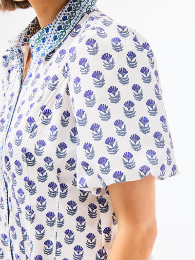 Woman wearing a dainty blue floral dress with a point collar and button front on a white background