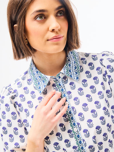 Woman wearing a dainty blue floral dress with a point collar and button front on a white background