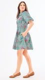 A woman standing in an elegant pose wearing a green floral dress with a classic point collar and bubble sleeves.