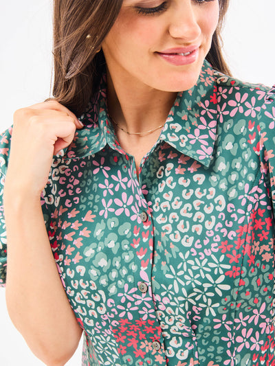 A woman standing in an elegant pose wearing a green floral dress with a classic point collar and bubble sleeves.