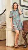 A woman standing in an elegant pose wearing a green floral dress with a classic point collar and bubble sleeves.