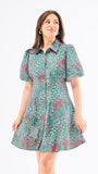 A woman standing in an elegant pose wearing a green floral dress with a classic point collar and bubble sleeves.