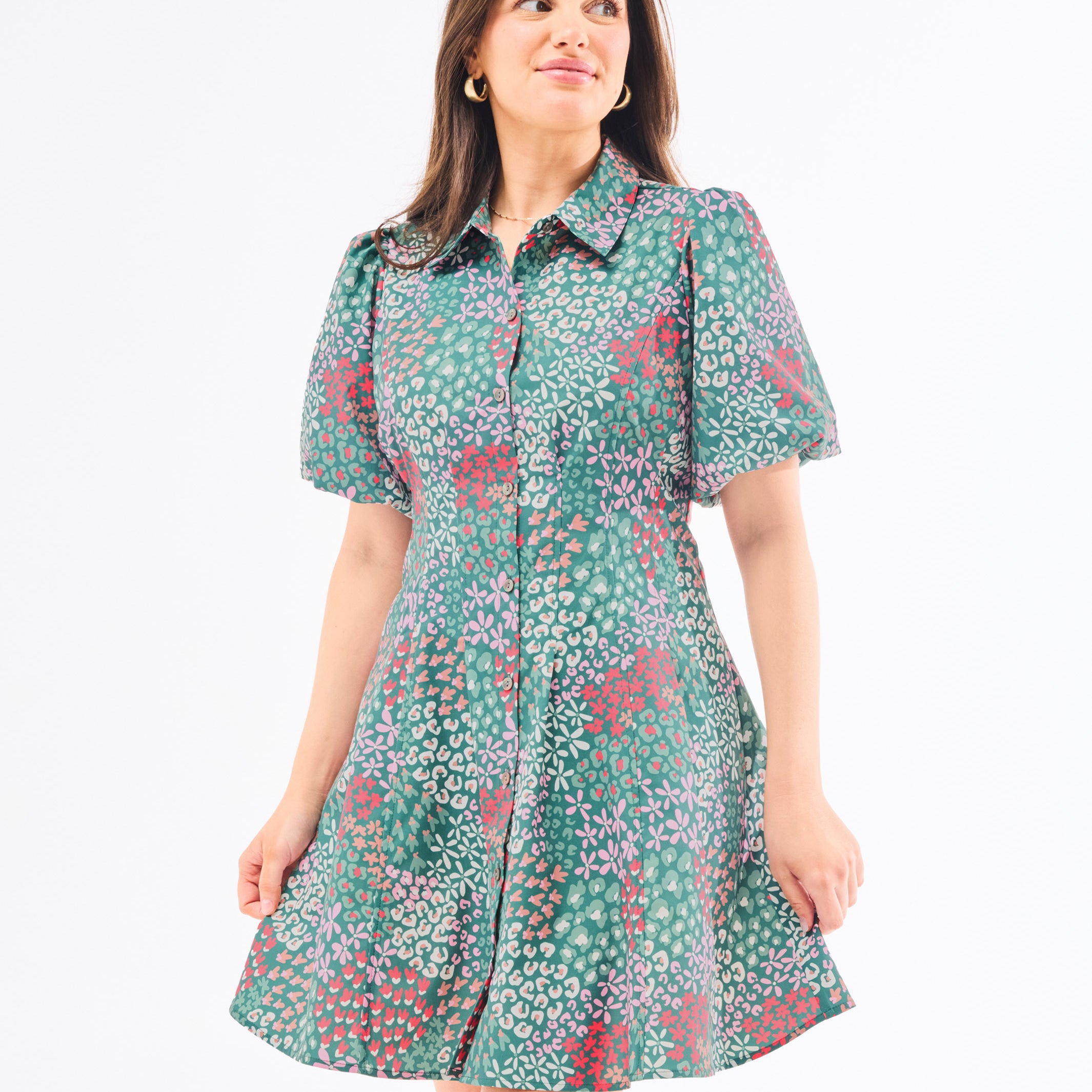 A woman standing in an elegant pose wearing a green floral dress with a classic point collar and bubble sleeves.