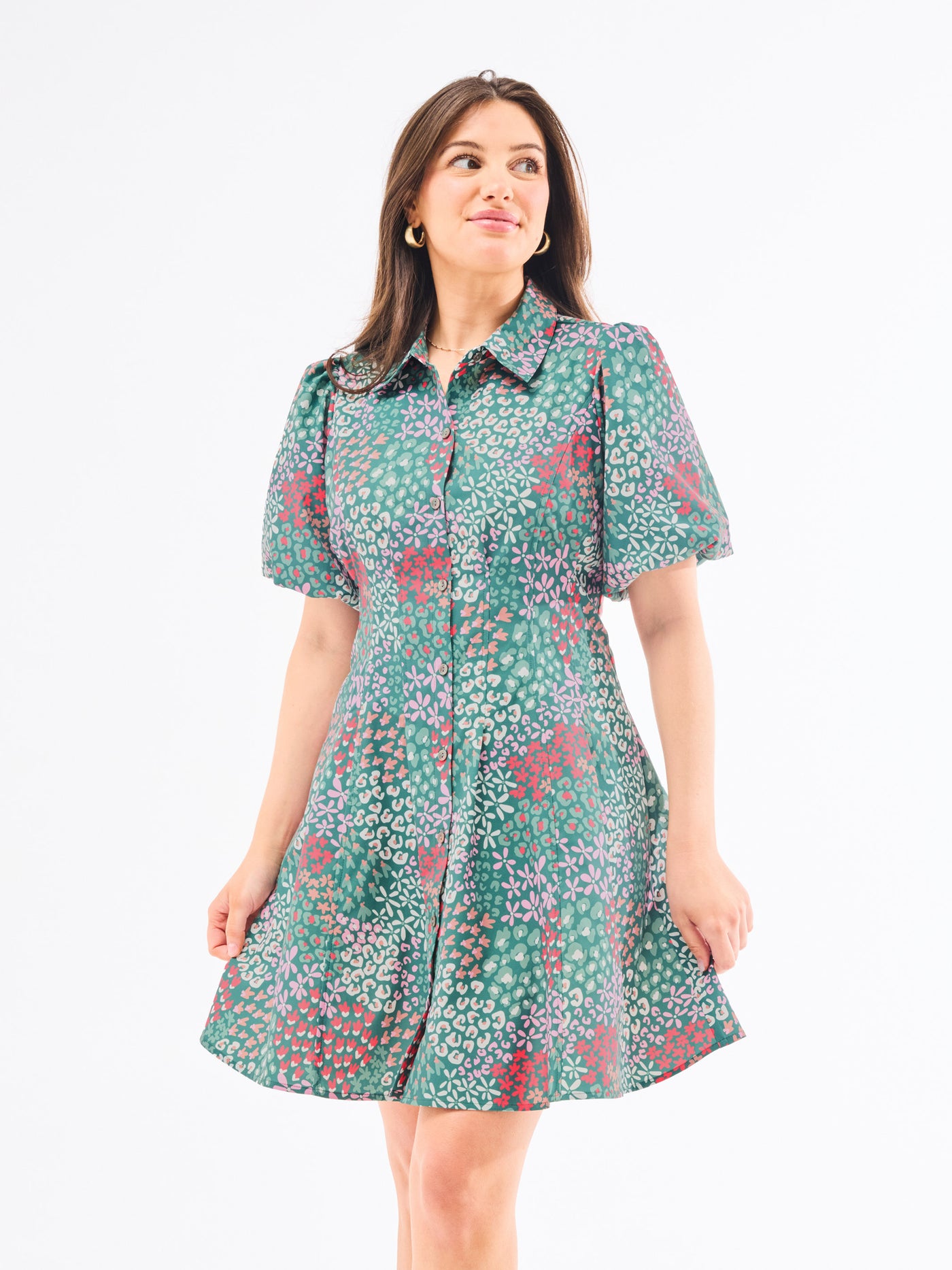 A woman standing in an elegant pose wearing a green floral dress with a classic point collar and bubble sleeves.