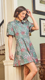 A woman standing in an elegant pose wearing a green floral dress with a classic point collar and bubble sleeves.