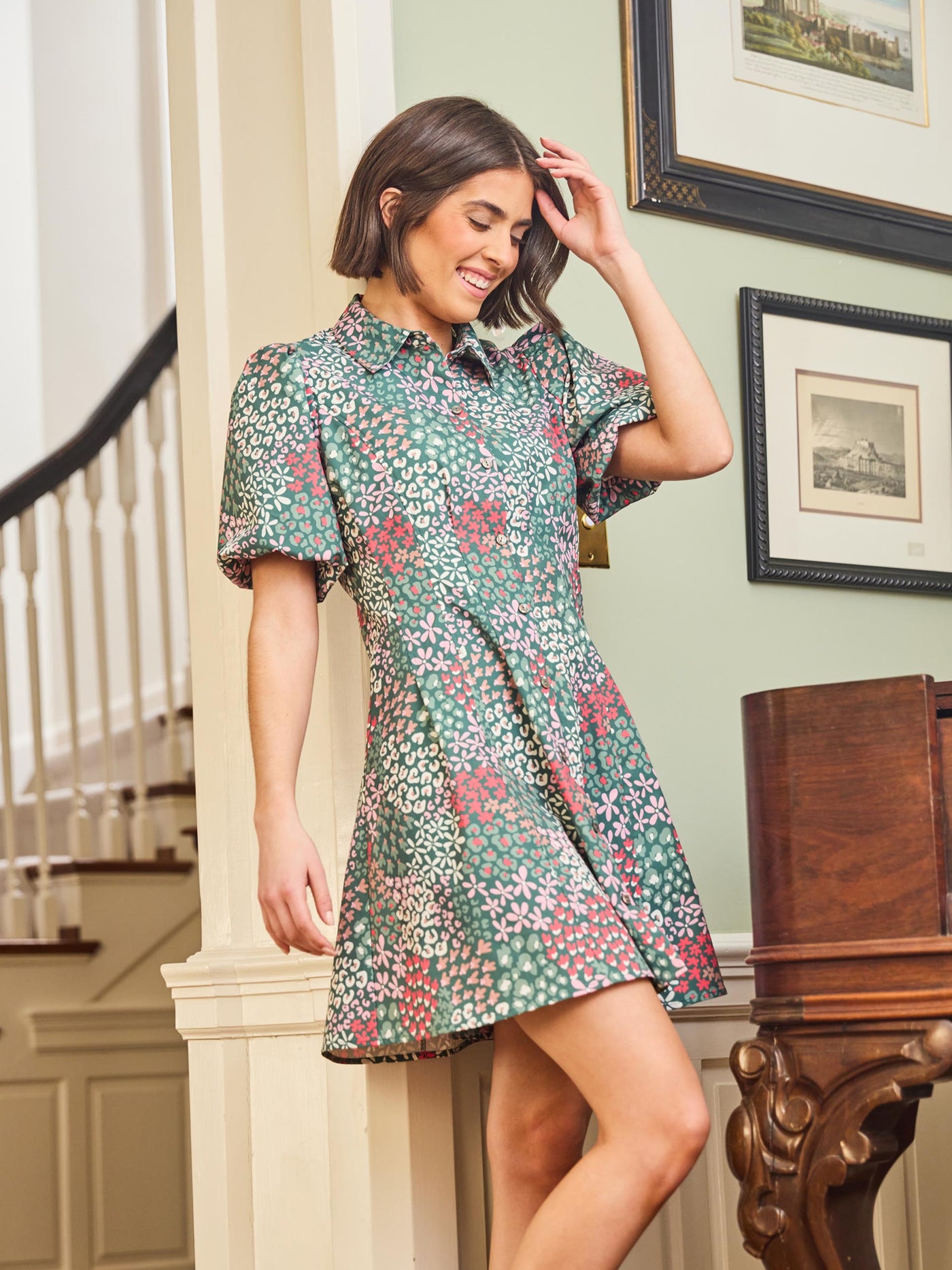 A woman standing in an elegant pose wearing a green floral dress with a classic point collar and bubble sleeves.