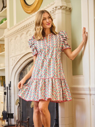 Woman in a floral dress standing in a room with a fireplace.