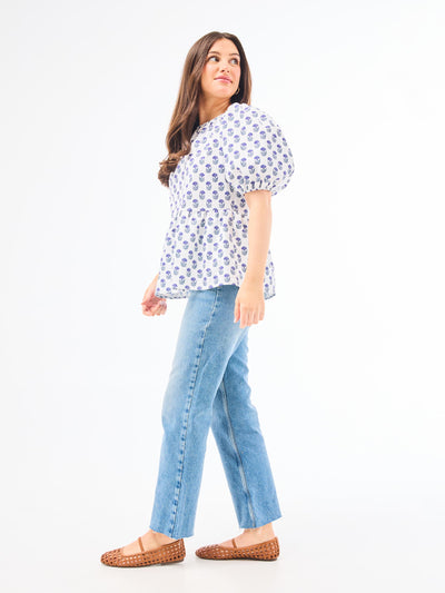 A woman wearing a floral foulard navy top with short puff sleeves and a jewel neckline.