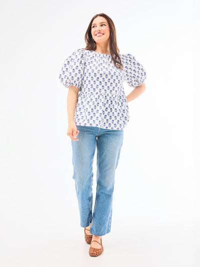 A woman wearing a floral foulard navy top with short puff sleeves and a jewel neckline.