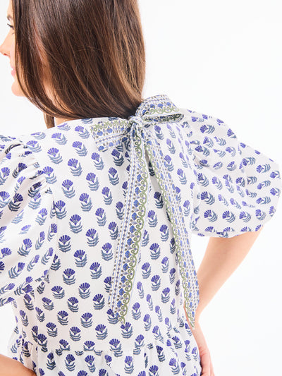 A woman wearing a floral foulard navy top with short puff sleeves and a jewel neckline.