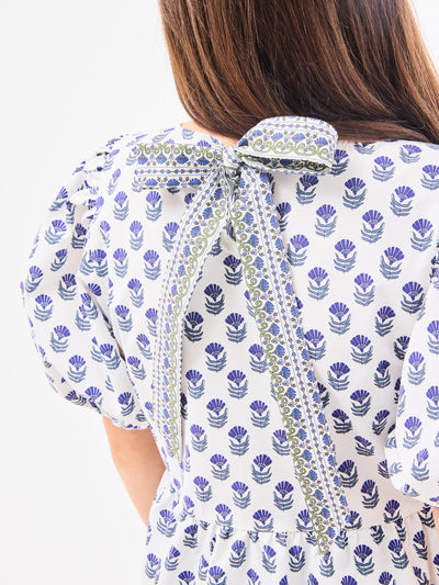 A woman wearing a floral foulard navy top with short puff sleeves and a jewel neckline.