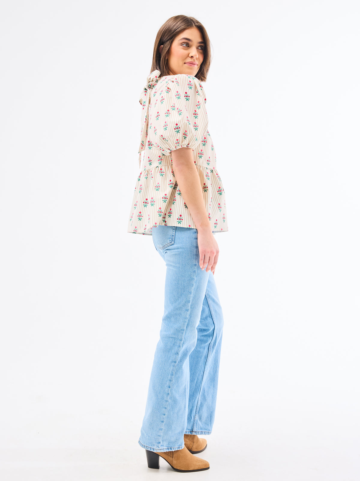 Woman wearing a floral blouse and light blue jeans on a white background