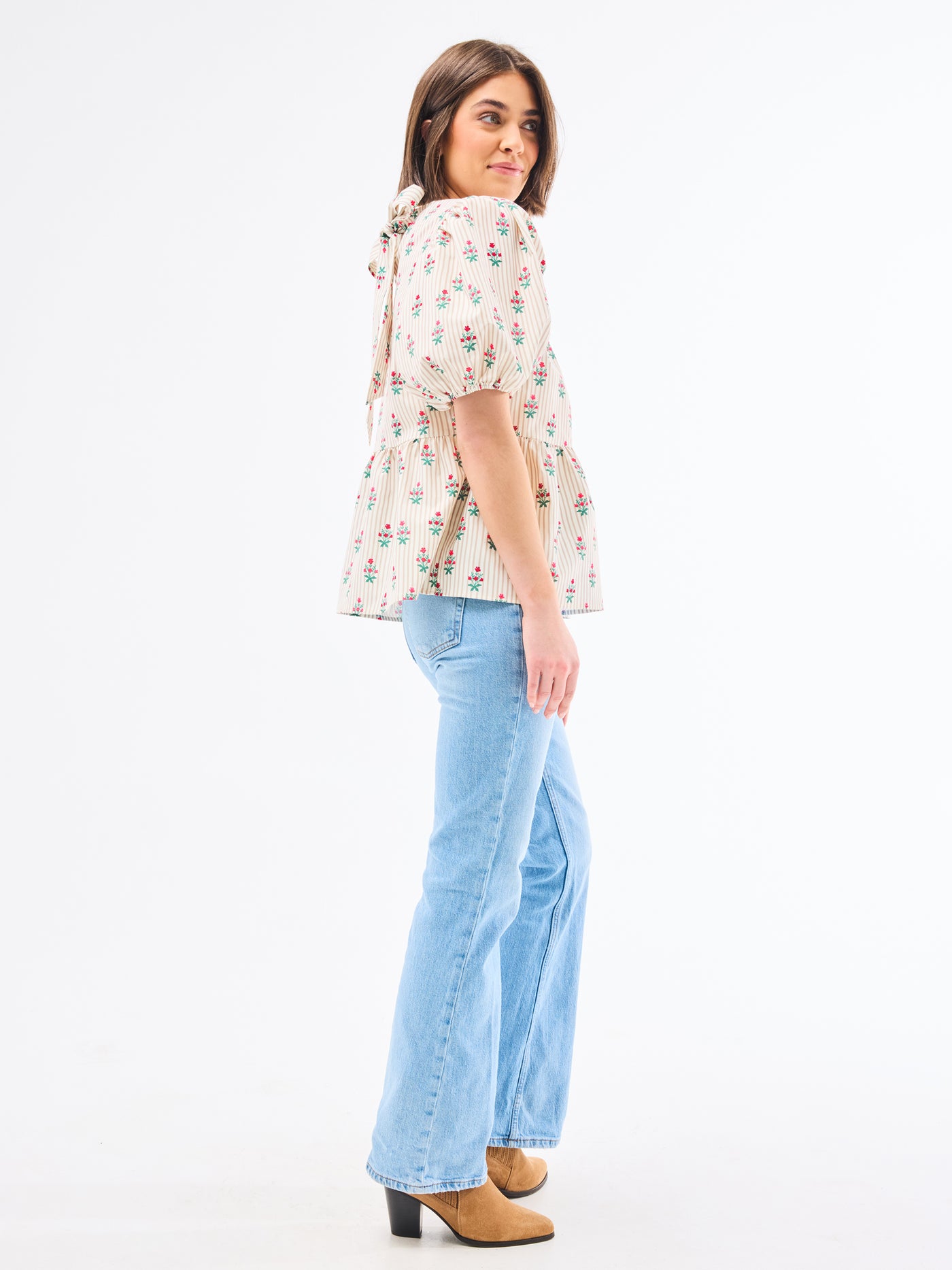 Woman wearing a floral blouse and light blue jeans on a white background