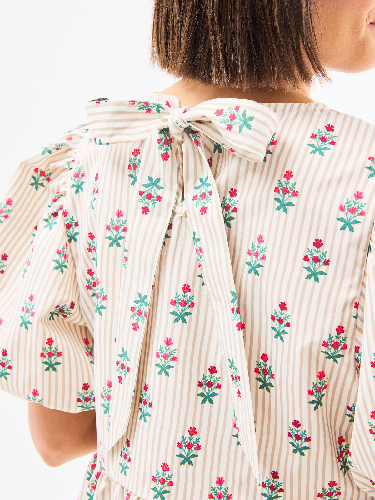 Close-up of a person wearing a floral dress with a bow detail on a white background