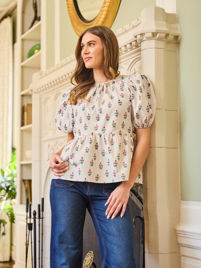 A woman wearing a beige top with a floral pattern, short puff sleeves, and elastic cuffs, paired with blue jeans.
