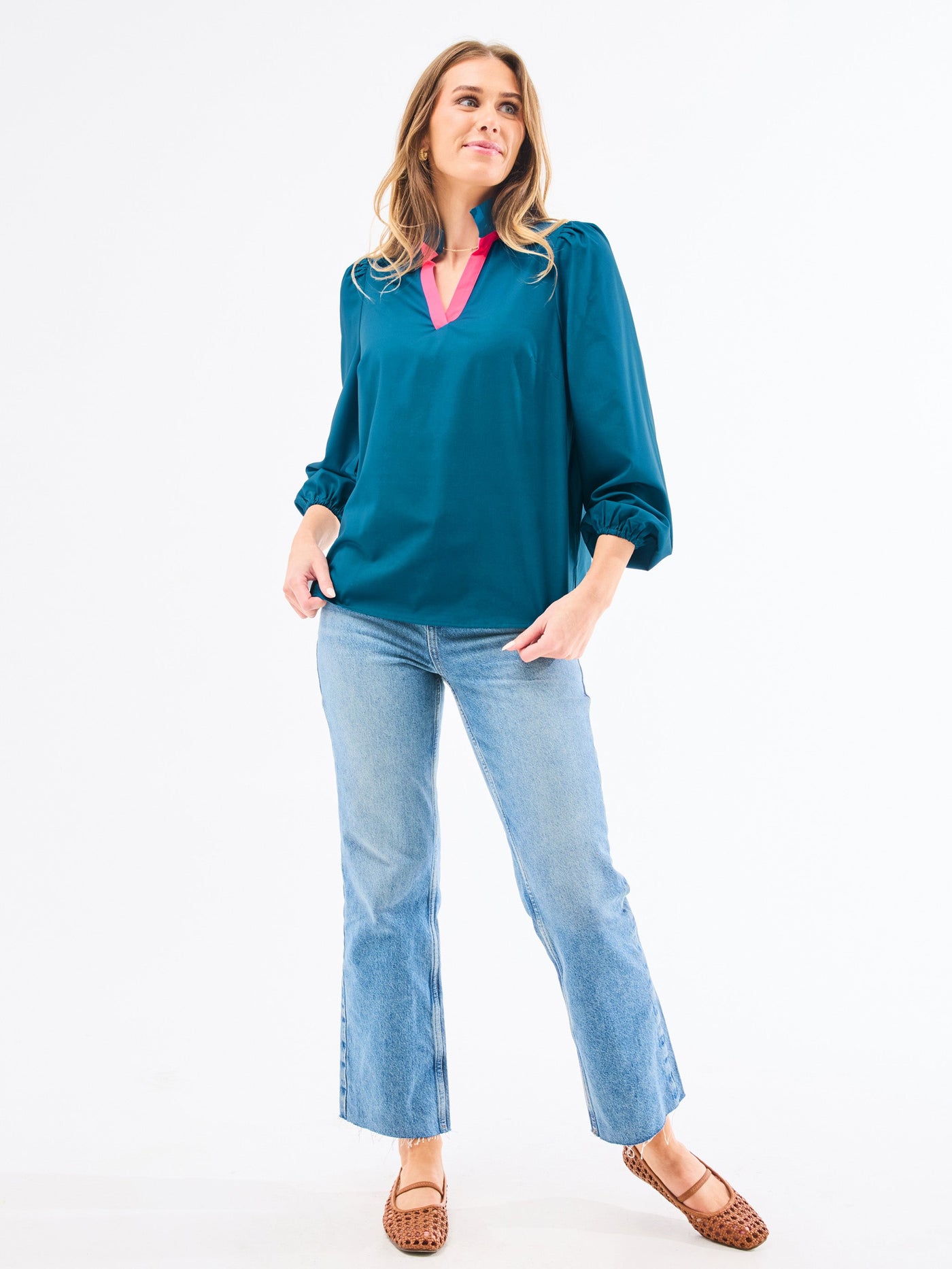Woman wearing a teal blouse with a pink collar and light blue jeans on a white background