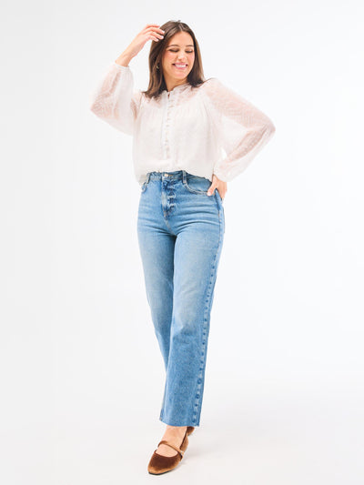A woman wearing a white long-sleeve top with a button-loop closure at the placket and elastic cuffs, paired with blue jeans.