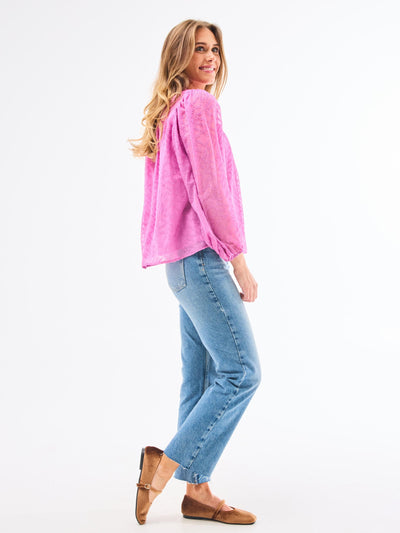 A woman modeling a pink long-sleeve top with a round neckline, paired with blue jeans and brown shoes.