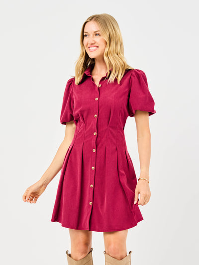 Woman wearing a red corduroy dress with puff sleeves and button front pintuck waist on a white background