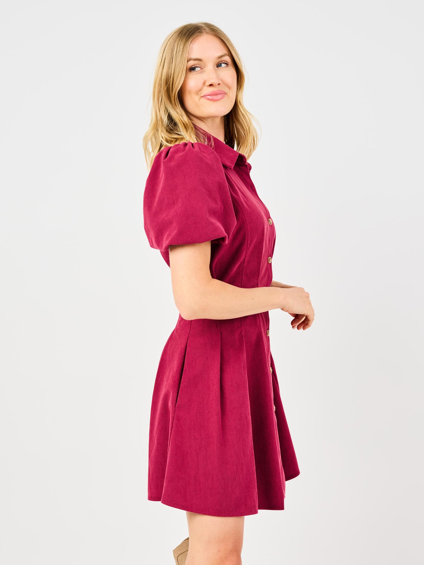 Woman wearing a red corduroy dress with puff sleeves and button front pintuck waist on a white background