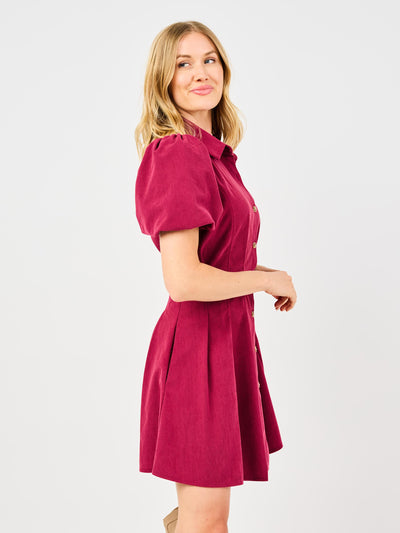 Woman wearing a red corduroy dress with puff sleeves and button front pintuck waist on a white background