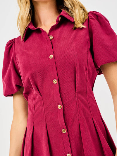 Woman wearing a red corduroy dress with puff sleeves and button front pintuck waist on a white background