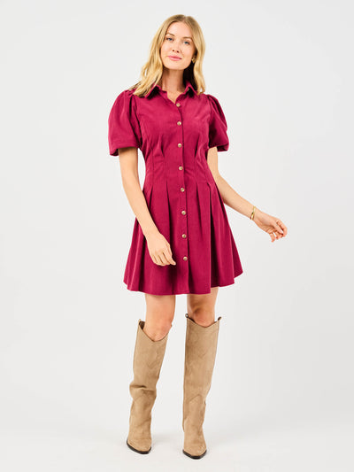 Woman wearing a red corduroy dress with puff sleeves and button front pintuck waist on a white background