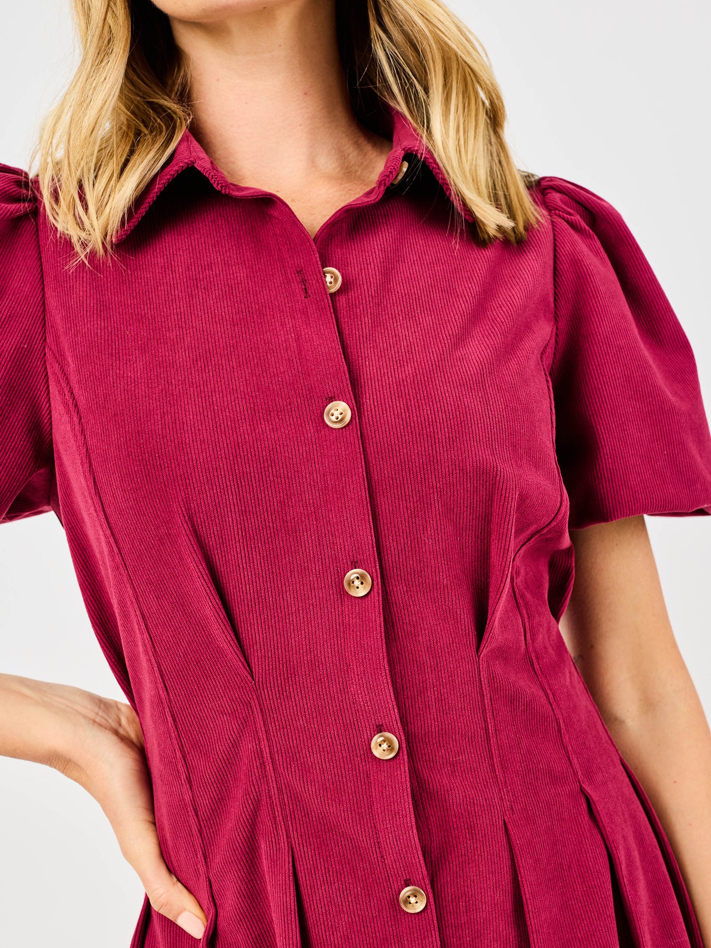 Woman wearing a red corduroy dress with puff sleeves and button front pintuck waist on a white background