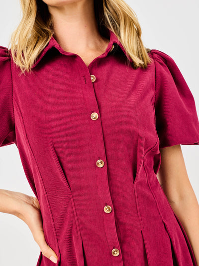 Woman wearing a red corduroy dress with puff sleeves and button front pintuck waist on a white background
