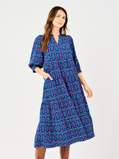 A model wearing a navy floral camouflage patterned dress with puff sleeves and elastic cuffs, paired with brown boots.