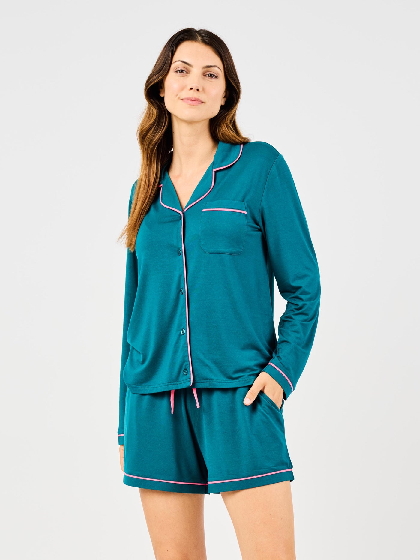 Woman wearing teal pajama set with pink piping on a white background