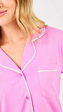 Close-up of a pink pajama top with white piping on a plain background