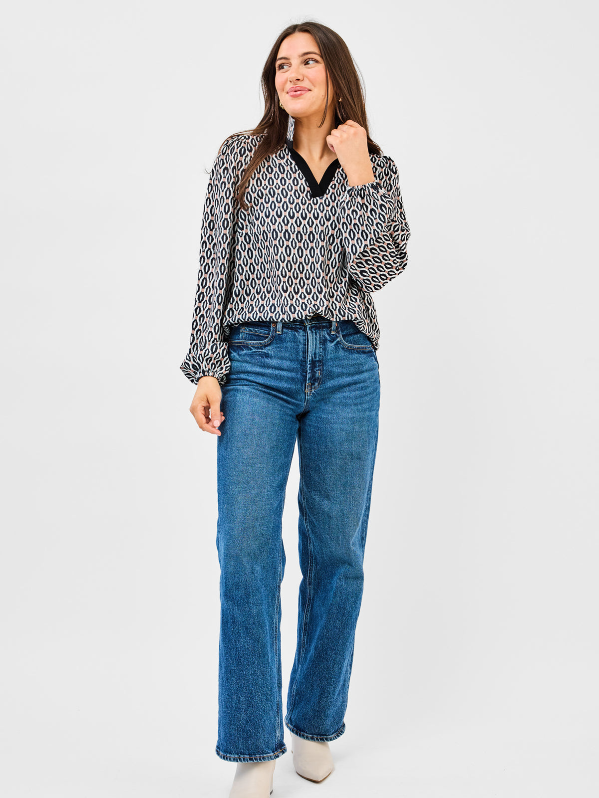 Woman wearing a patterned blouse and blue jeans on a white background