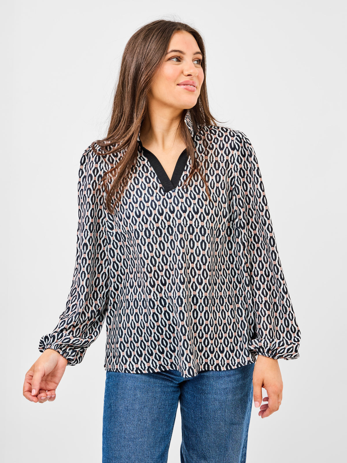 Woman wearing a patterned blouse and jeans on a plain background