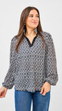 Woman wearing a patterned blouse and jeans on a plain background