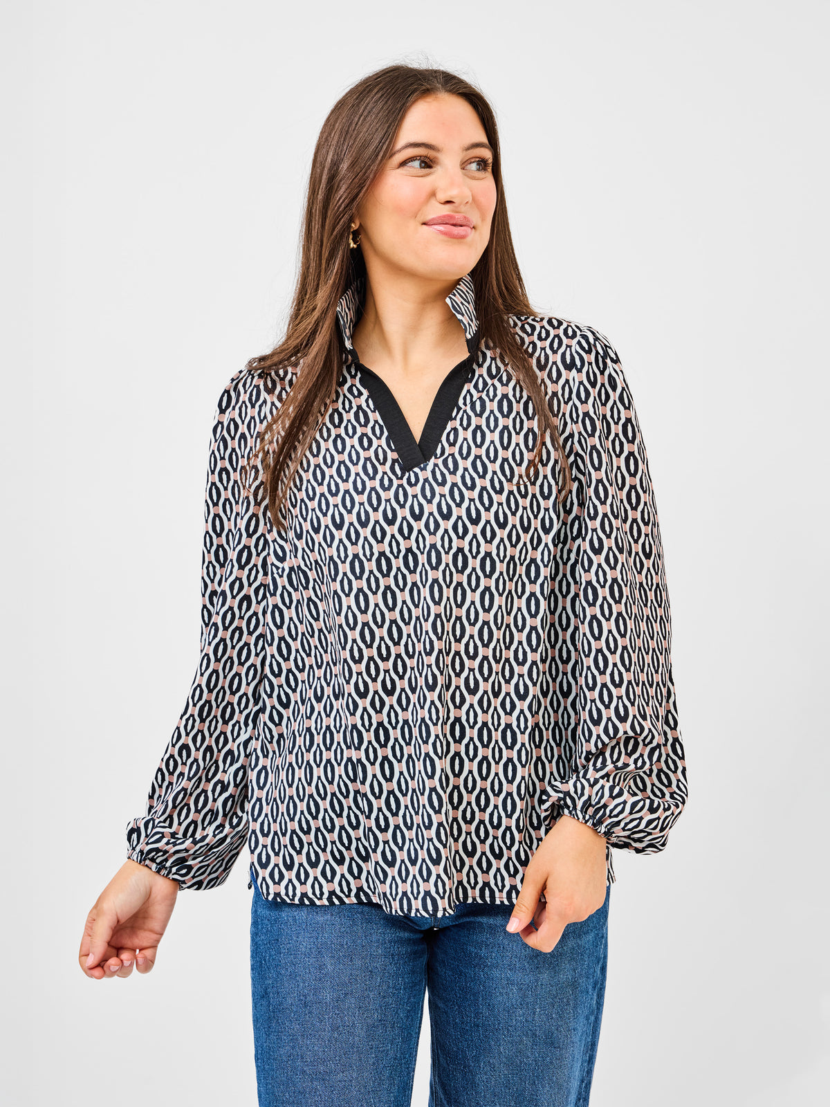 Woman wearing a patterned blouse and jeans on a plain background