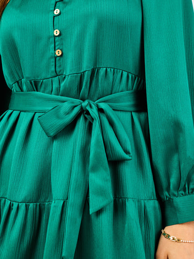 Green dress with a tie waist and button details on a blurred background