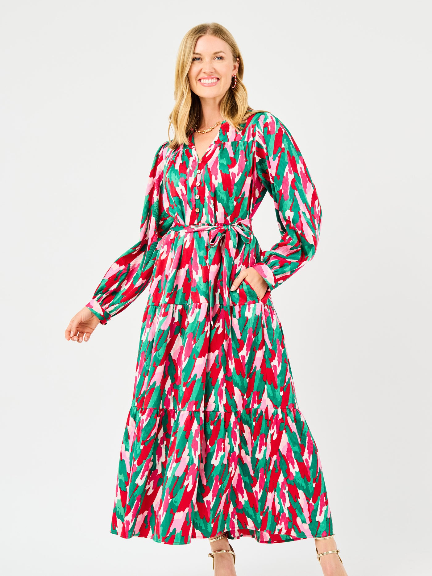 Woman wearing a colorful patterned holiday dress with pinks, greens, reds and whites on a white background